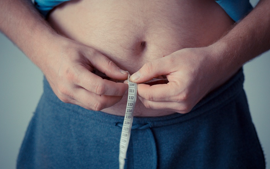 muž s nadváhou si měří metrem obvod kolem břicha