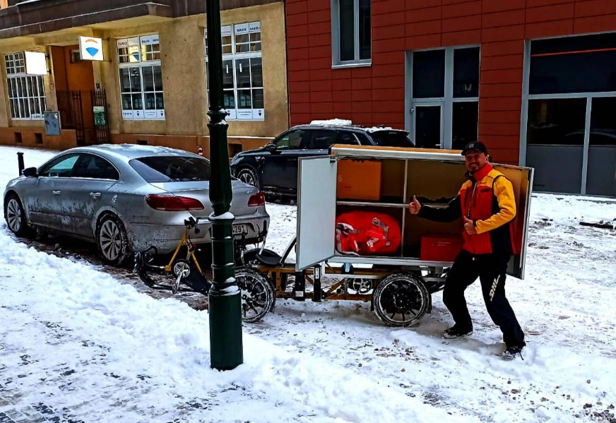 cyklokurýr stojící v zasněžené Praze před svým nákladním kolem