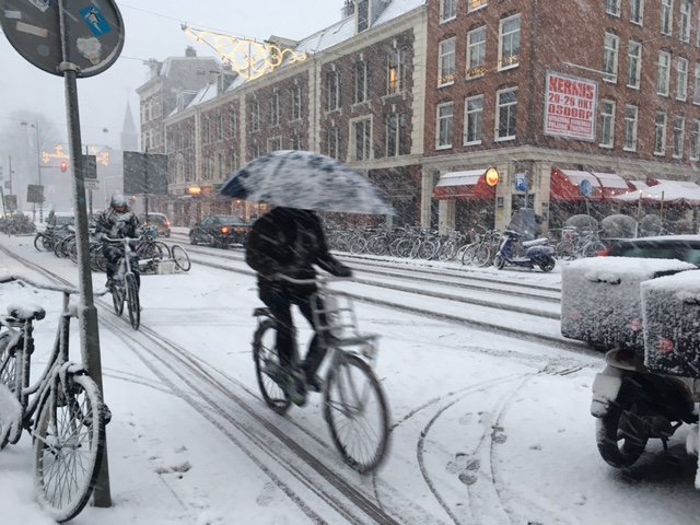 cyklisté v Nizozemsku jedou ve velkém počtu na sněhu, jeden má nad hlavou deštník
