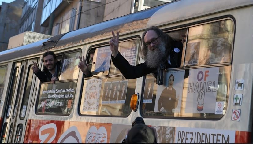 Foto jedoucí tramvaje Václava Havla, z okna vyklonění cestující ukazují prsty "viktorku"