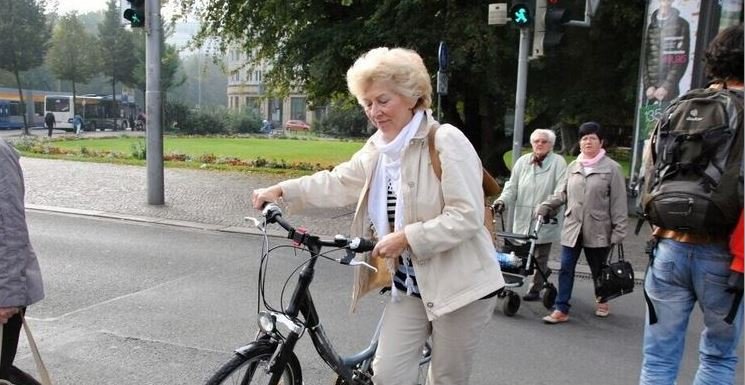 starší paní vede kolo, okolo chodci
