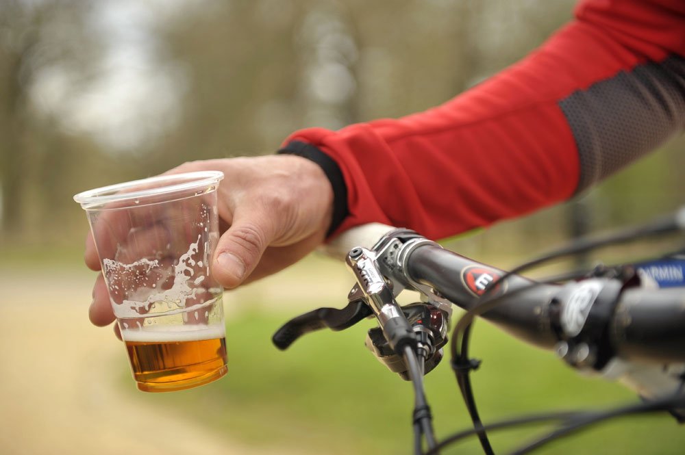 Cyklista drží na řidítkách kola kelímek piva