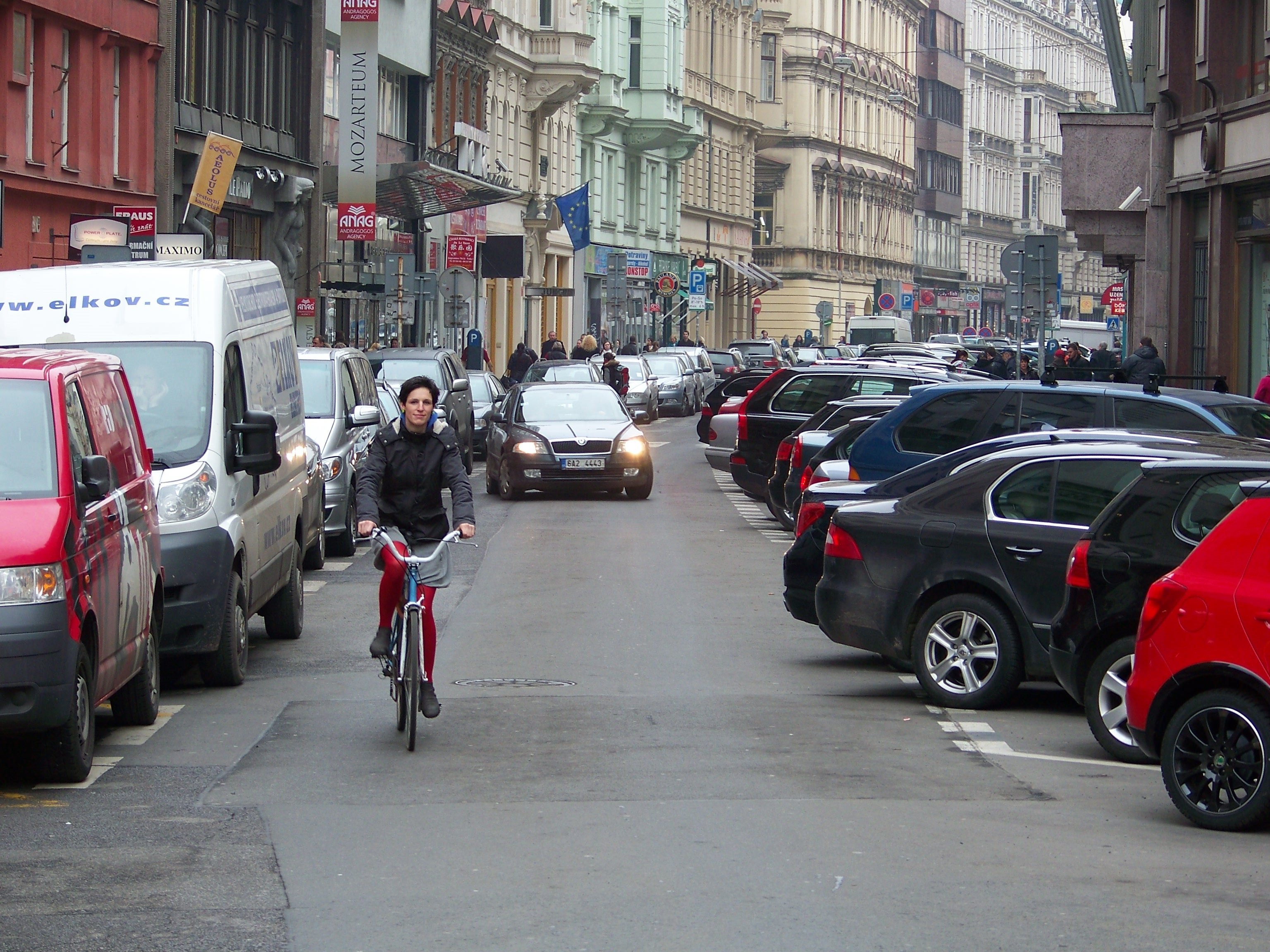 pražská ulice se zaparkovanými auty, po níž jede kolo