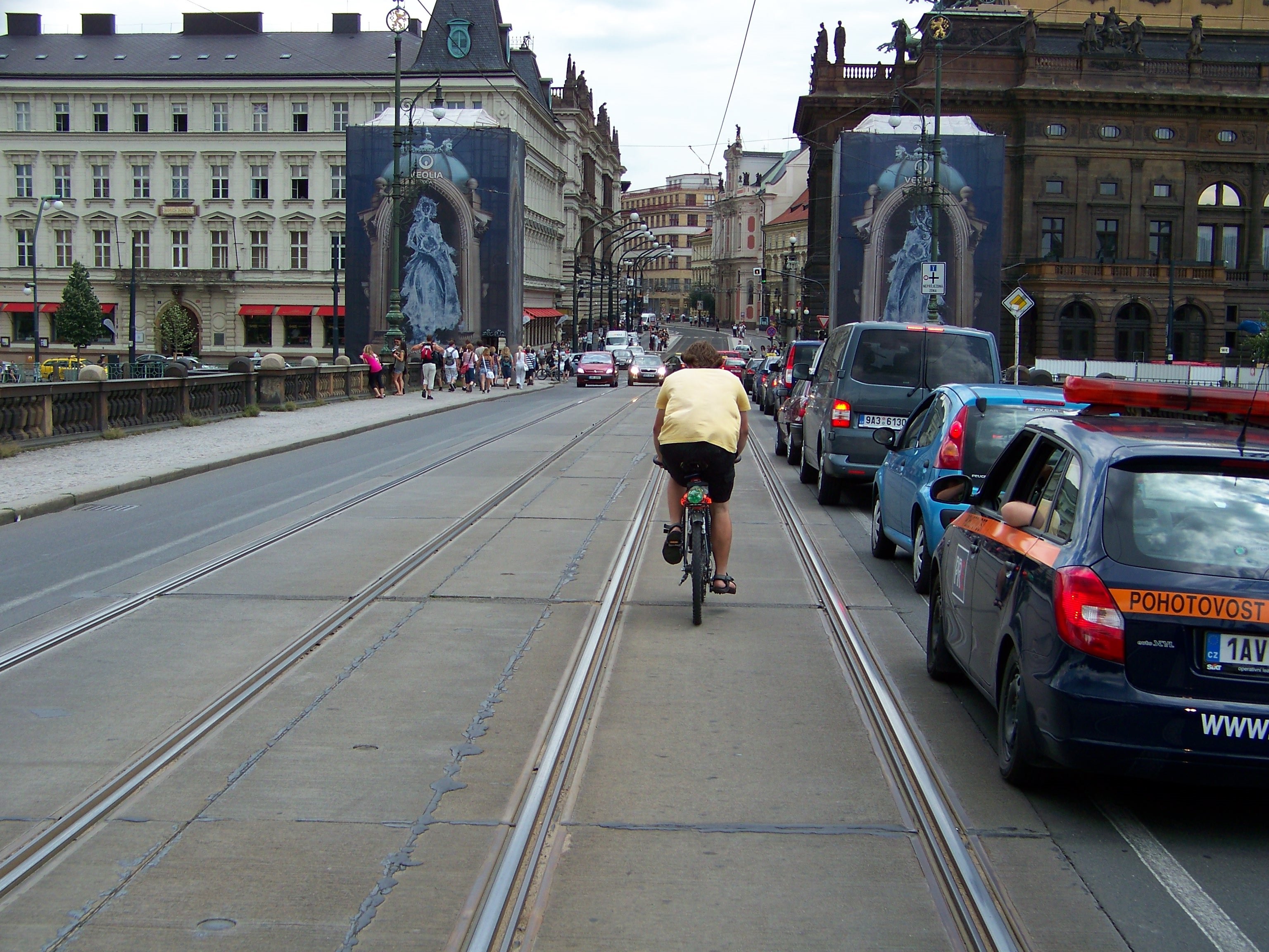 CYKLISTA PŘEDJÍŽDÍ POMALU SE SUNOUCÍ KOLONU VELVO PO TRAMVAJOVÝCH KOLEJÍCH