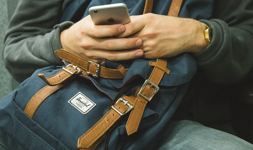 sedící cestující, na kolenou má batoh a v ruce mobilní telefon