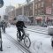 cyklisté v Nizozemsku jedou ve velkém počtu na sněhu, jeden má nad hlavou deštník